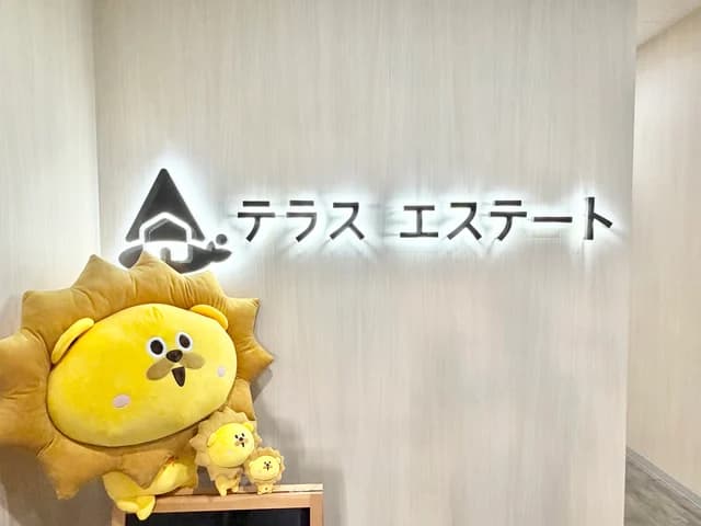 テラスエステート熊本本店のエントランス。壁の社名ロゴサインの下に、マスコットのぬいぐるみが3体置かれている